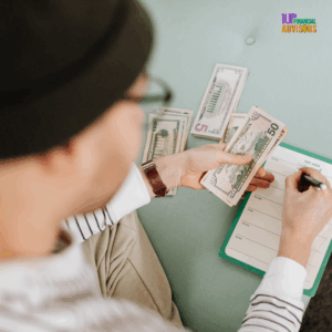 Content creator budgeting cash with a weekly planner, organizing expenses with $50 and $5 bills, seated casually with notepad on lap — 1UP Financial Advisors branding visible.